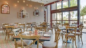 Un restaurante con sillas y mesas de madera, ventanas amplias y lámparas colgantes.