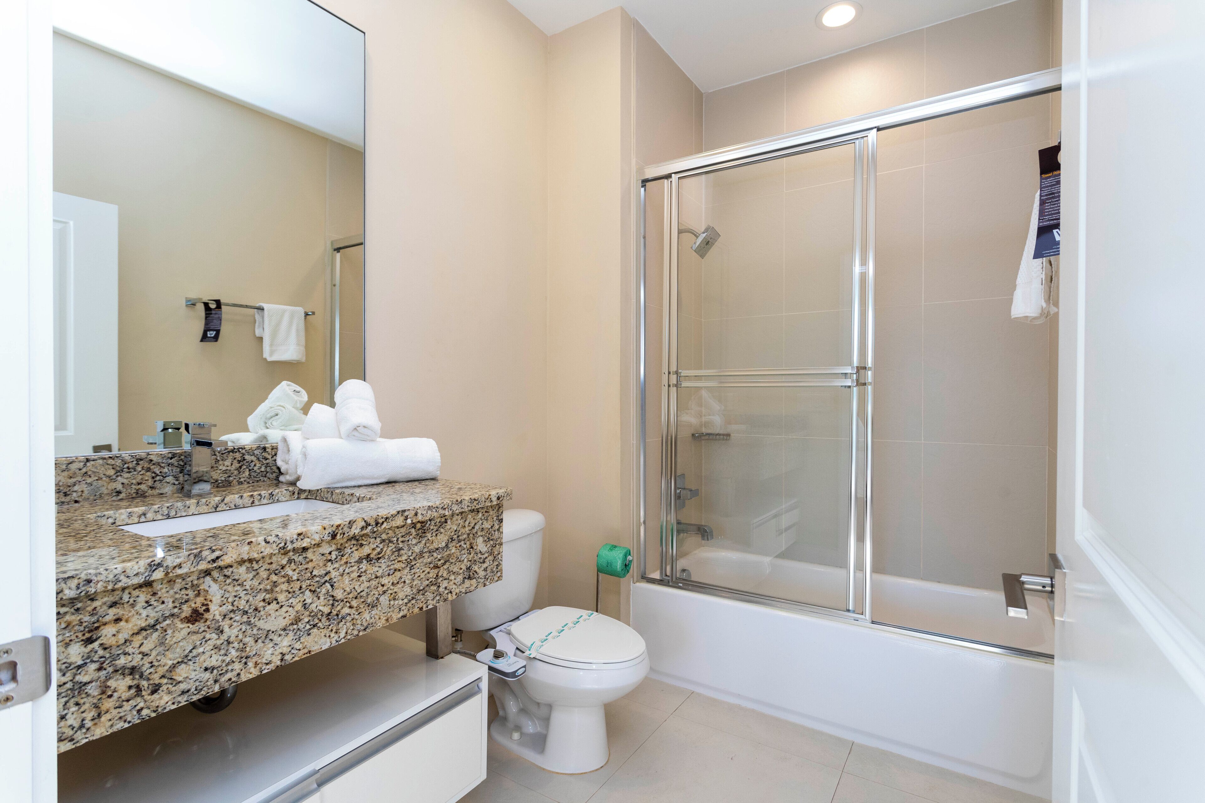 A modern bathroom with a granite countertop, a toilet, a glass-enclosed shower, and a bathtub.