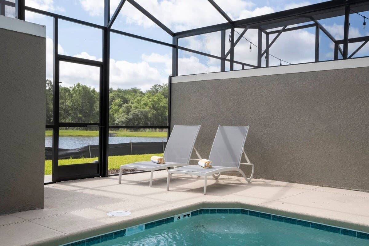 An indoor pool area with two lounge chairs and a view of a lake.