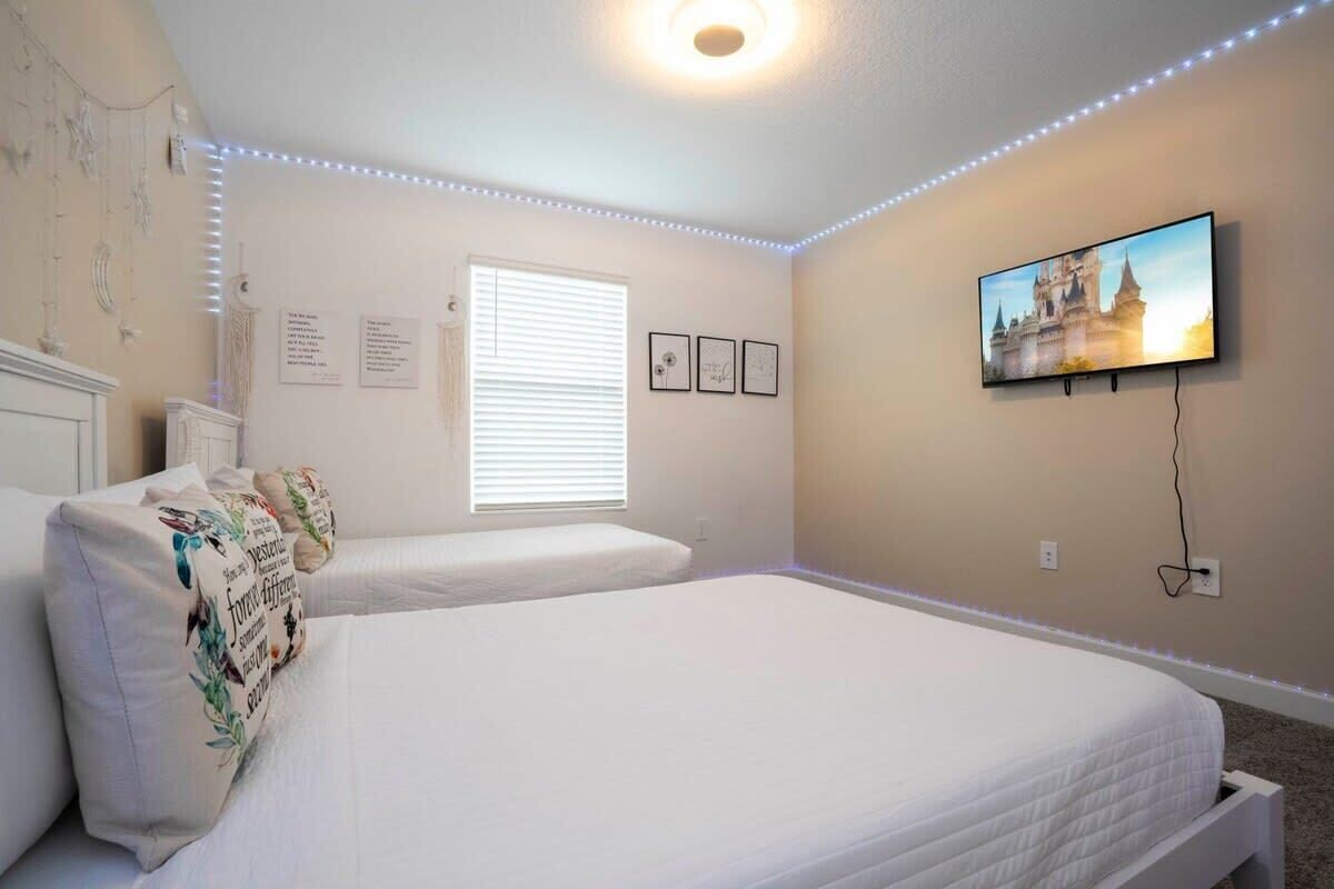 A bedroom with two beds, a TV mounted on the wall, and decorative lights along the ceiling.