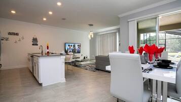 Cozinha moderna com armários brancos, uma ilha central e um espaço de refeições com mesa e cadeiras brancas.