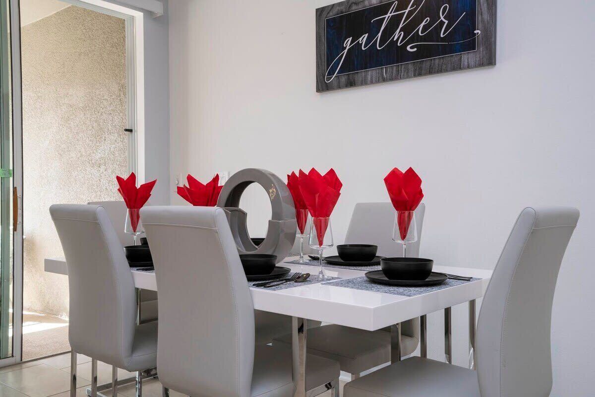 Een eettafel, voorzien van witte stoelen, zwart servies en rode servetten. Een bordje aan de muur met de tekst 'gather'.