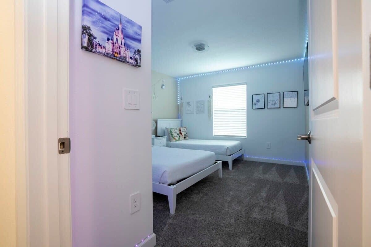 A bedroom with a bed, a nightstand, a window, and LED strip lights along the ceiling.