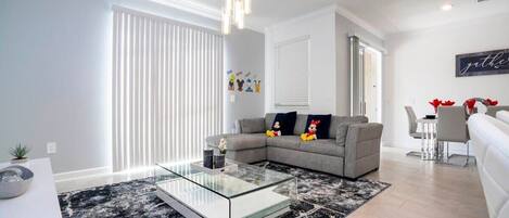 A modern living room with a glass coffee table, grey sofa, and a black and white rug.