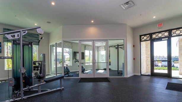 Een sportschool met trainingsapparatuur, een spiegelwand en uitzicht door glazen deuren.