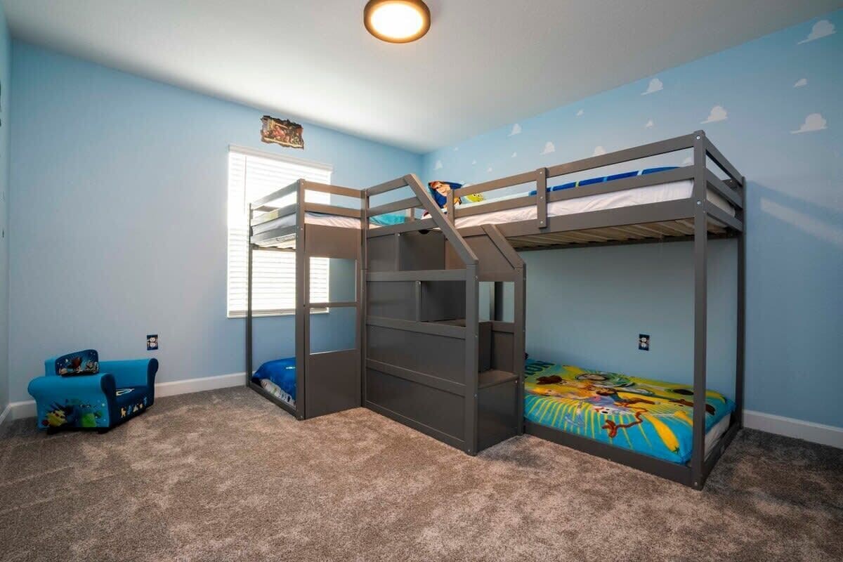 Een slaapkamer met stapelbed, raam, een blauwe stoel en een wand met een wolkendesign.