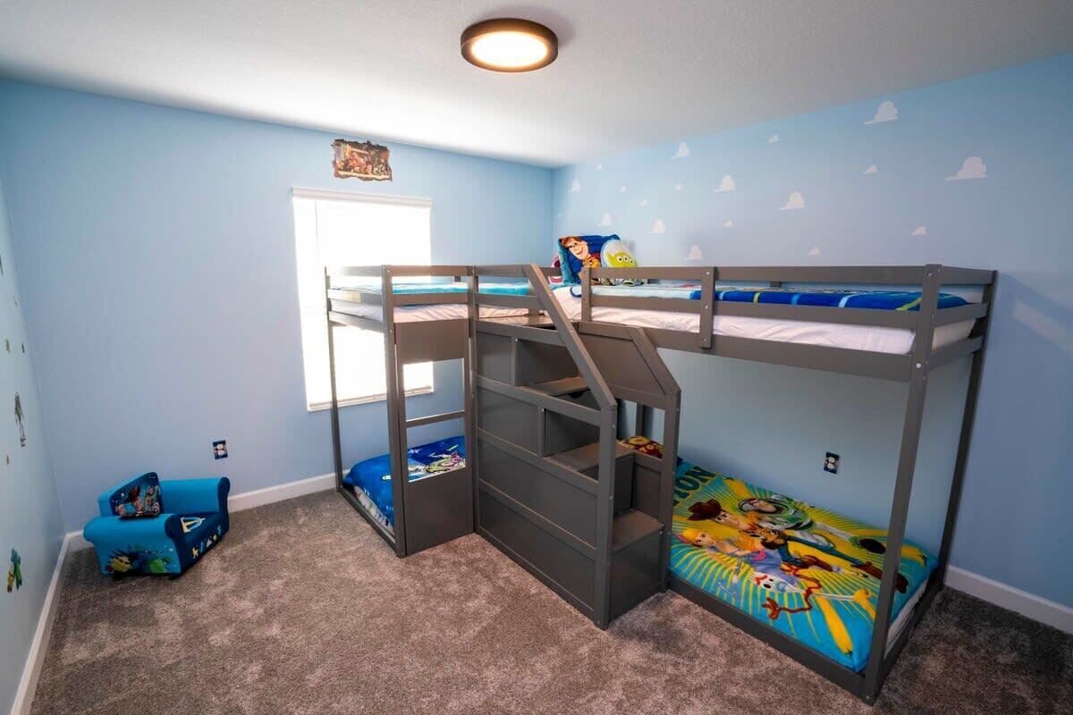 A bunk bed room with a window, a small blue chair, and a wall decal.