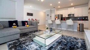 Ein modernes Wohnzimmer mit grauem Sofa, Glastisch und Teppich in Schwarz und Weiß.