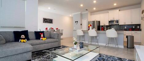 A modern living room with a grey sofa, glass coffee table, and a black and white rug.