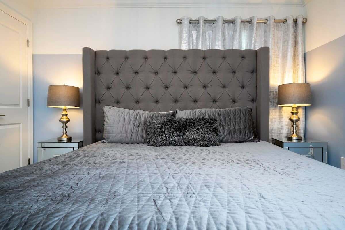Une chambre à coucher avec une tête de lit capitonnée, deux lampes de chevet et une couvre-lit matelassé.