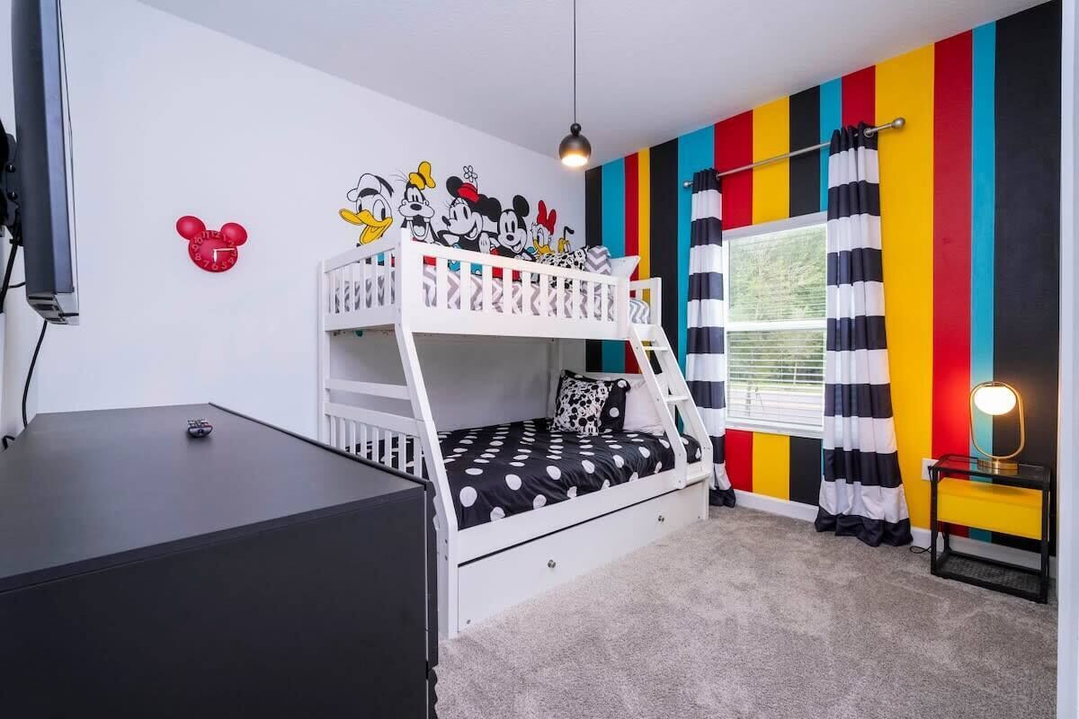 A bunk bed room with a Mickey Mouse wall decal, a TV, and a window with striped curtains.