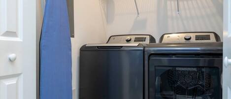 A laundry area with a washing machine and dryer, a blue towel hanging on a rack, and a shelf with laundry supplies.