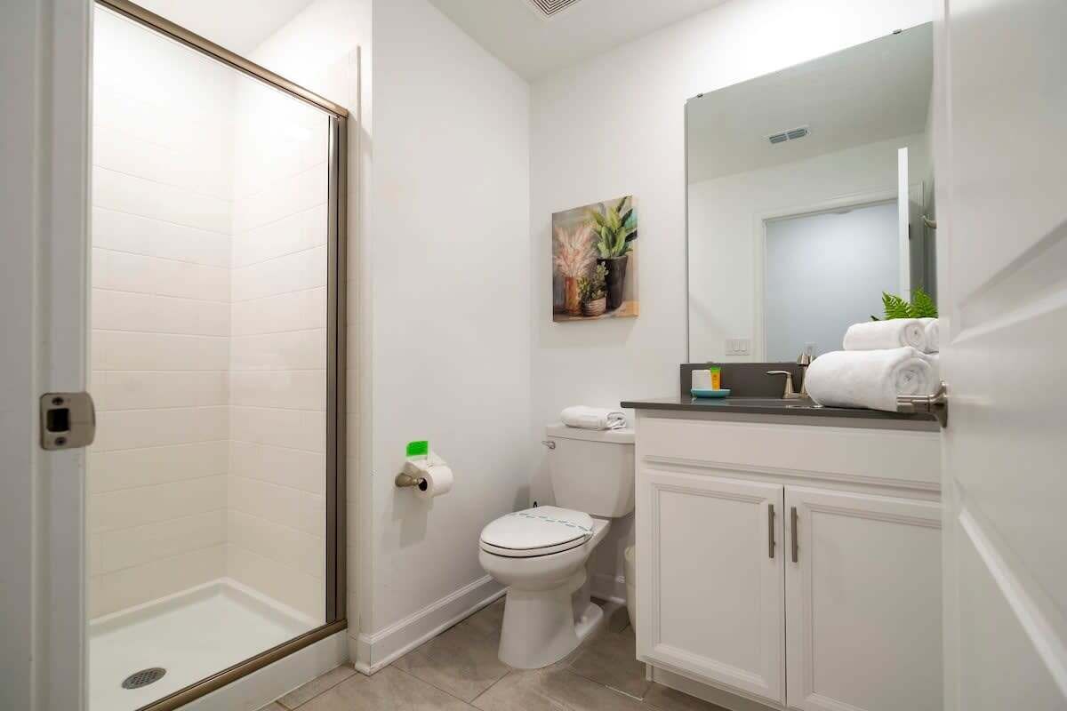 A bathroom with a glass shower enclosure, a toilet, a sink with a mirror, and a small potted plant on the wall.