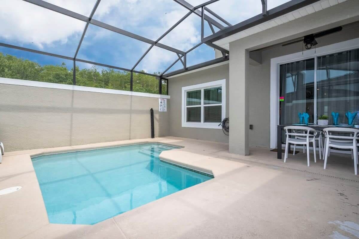 A swimming pool with a glass enclosure, a dining area with chairs, and a window with blinds.