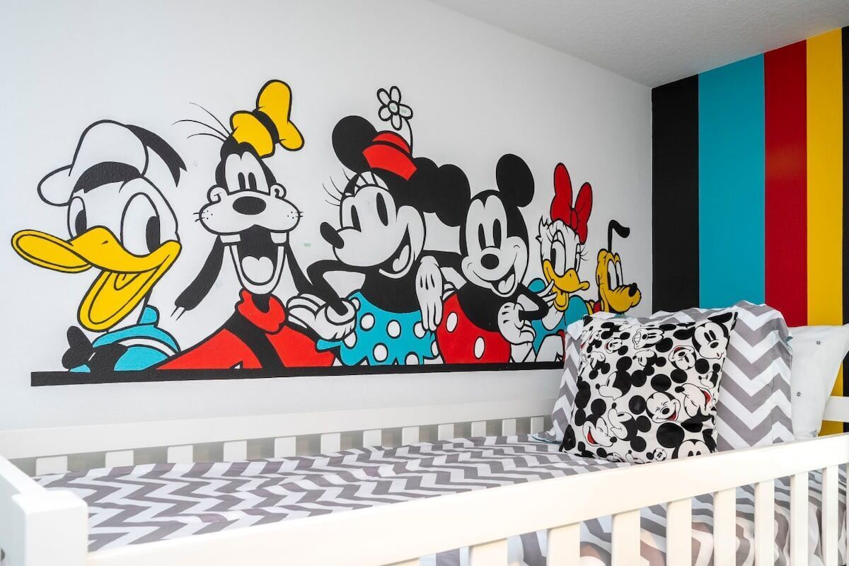 A baby room with a crib, a colorful wall mural, and a patterned bedspread.