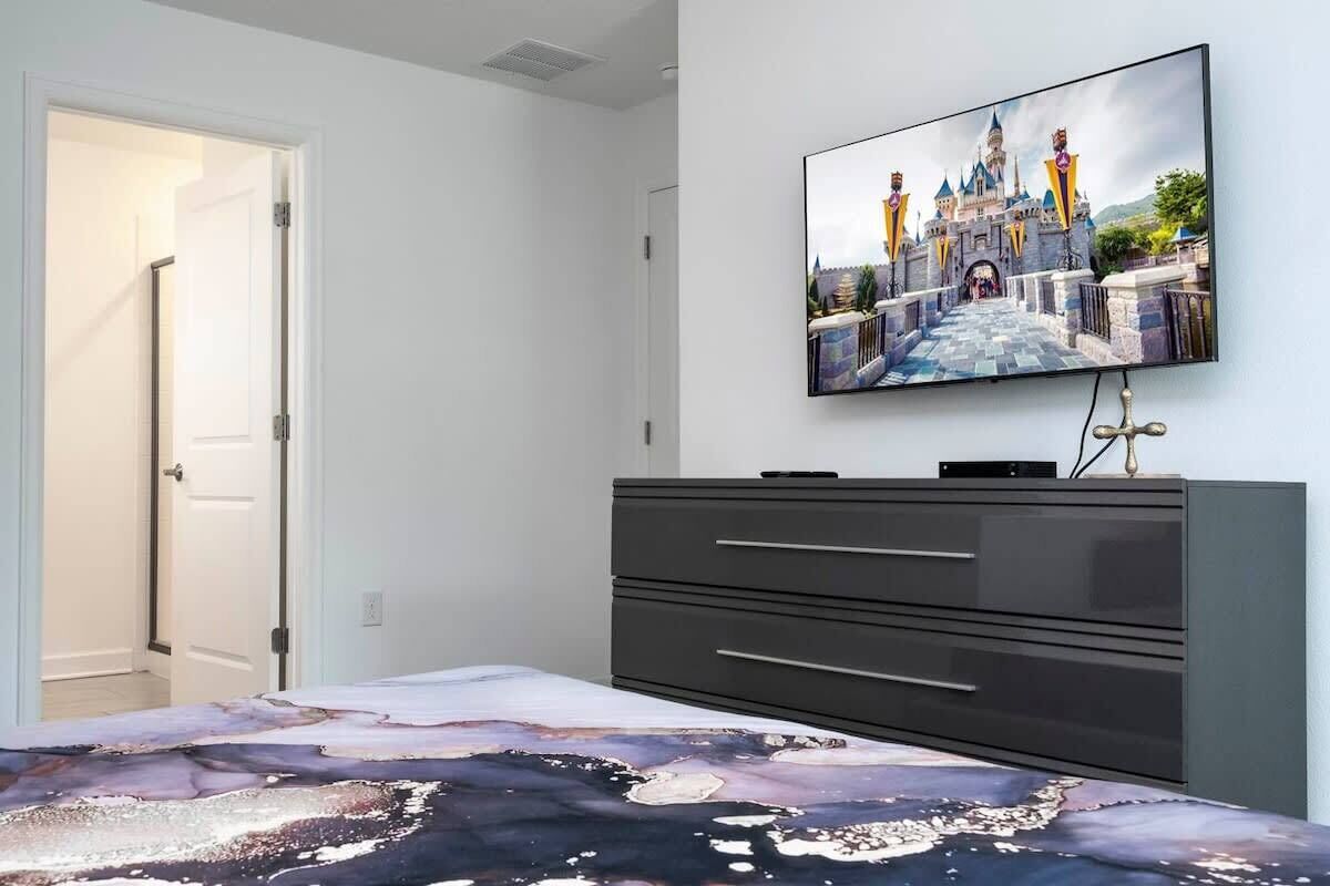 A bedroom with a bed, a dresser, and a TV on the wall displaying a castle image.