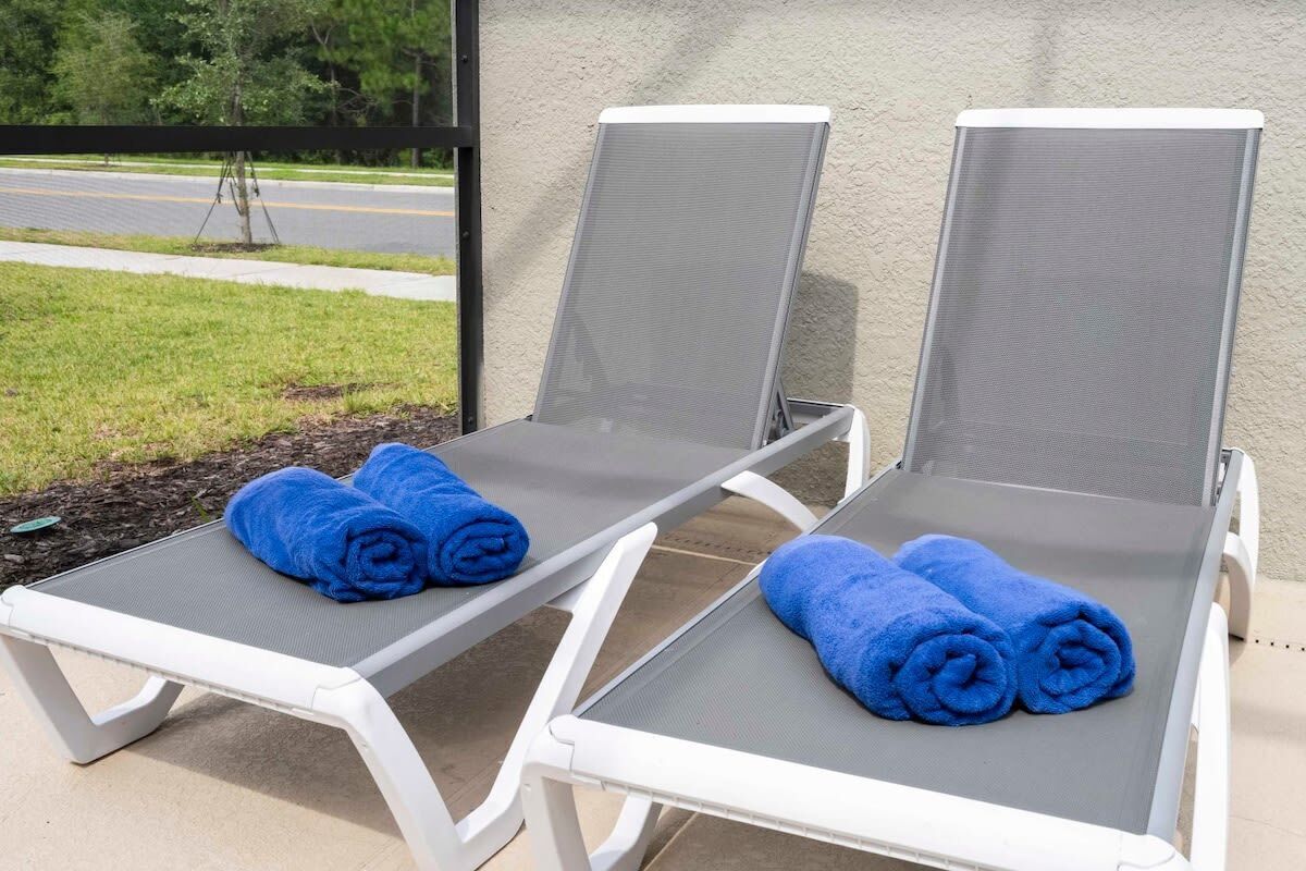 Two sun loungers with grey mesh backs and white frames, each with a rolled blue towel on top.