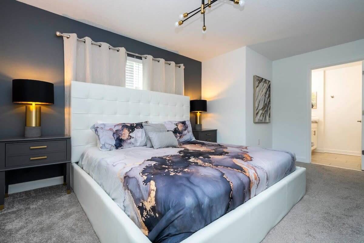 Une chambre à coucher moderne avec un grand lit, deux tables de chevet avec des lampes, une tête de lit et un tableau au mur.