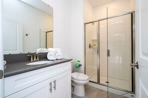 A modern bathroom with a white vanity, a large mirror, a glass shower enclosure, and a toilet.