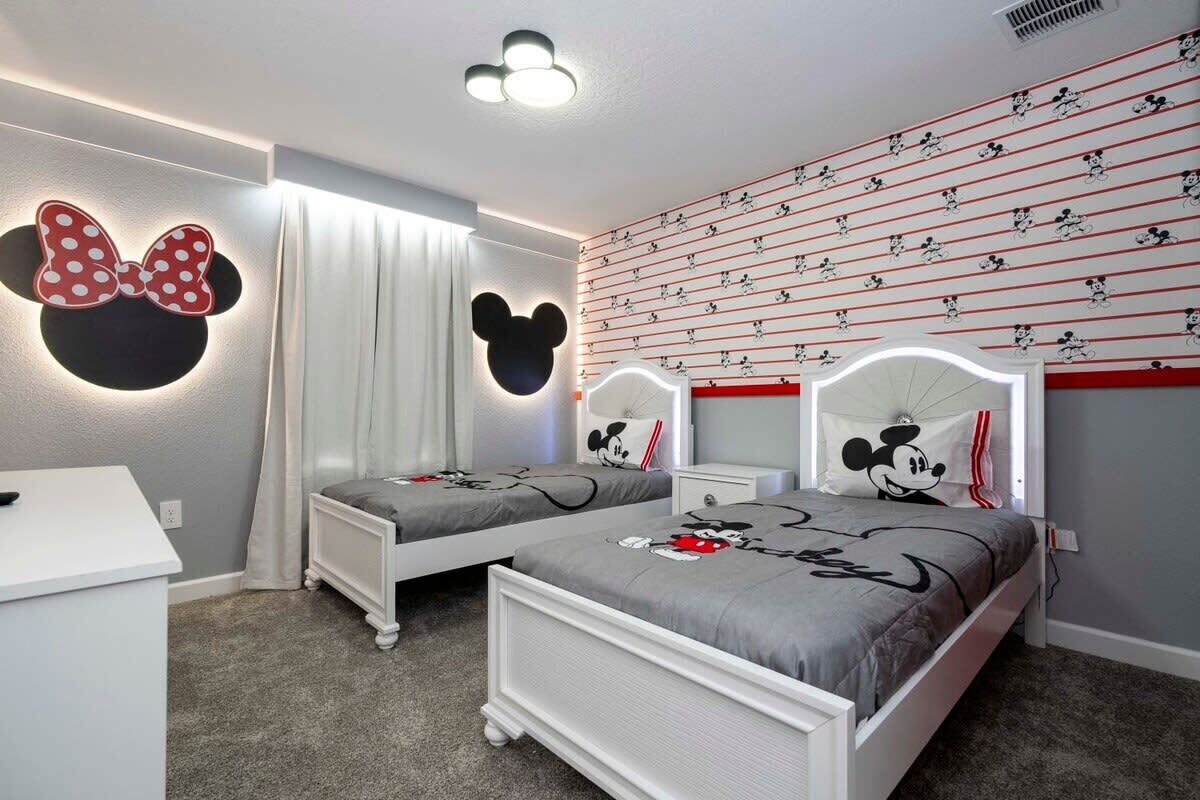 Un dormitorio con dos camas, un escritorio y decoración temática de Mickey Mouse.