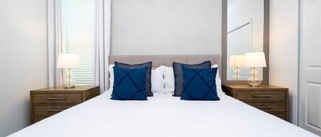 A hotel room with a large bed, two bedside tables with lamps, a mirror, and a window with curtains.