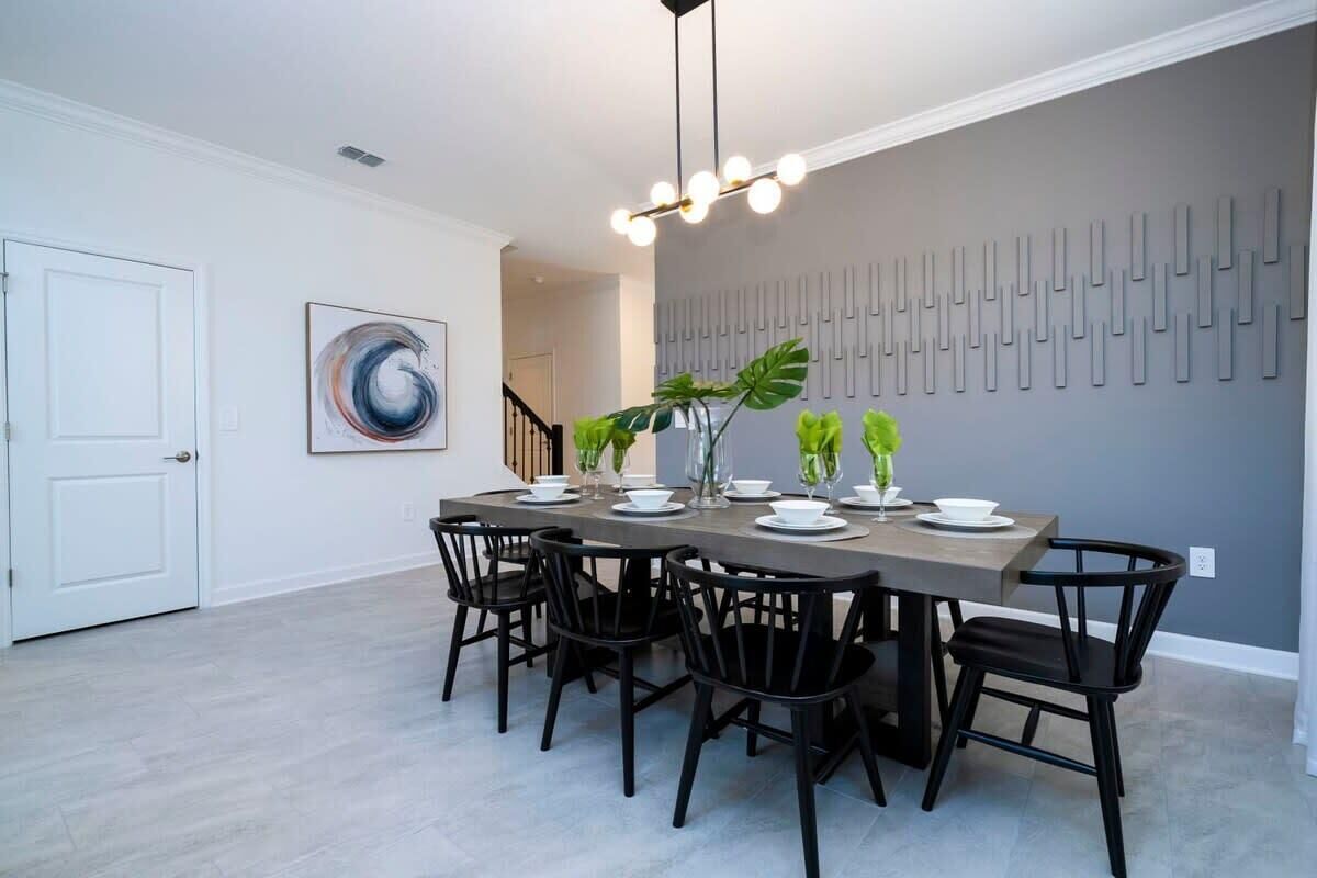 A dining area with a rectangular table, black chairs, a modern chandelier, and a wall-mounted abstract art piece.