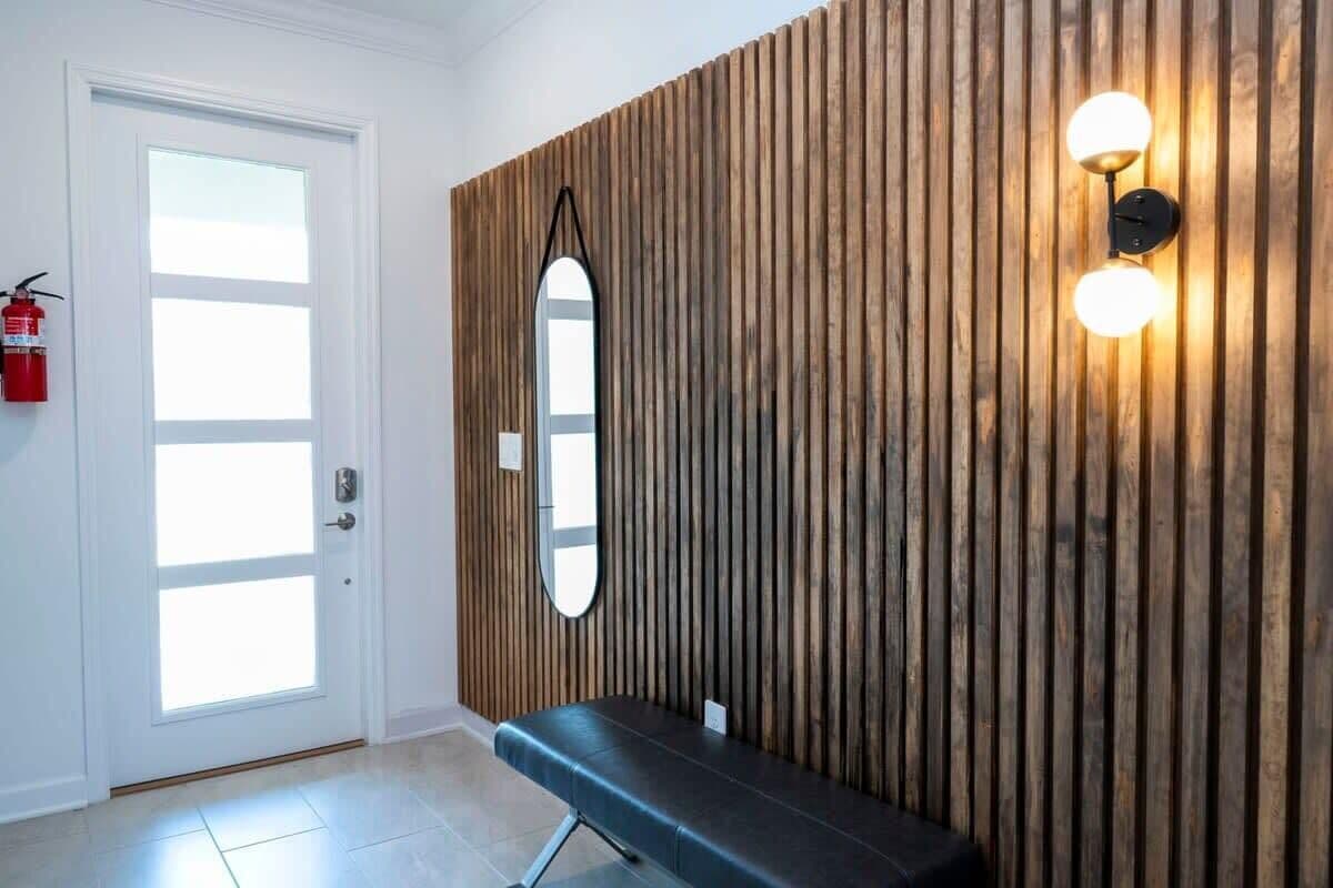 A room with a wooden panel wall, a bench, a mirror, and a wall-mounted light fixture.