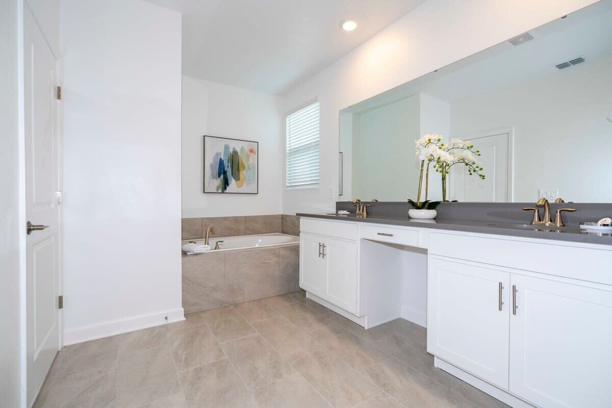 A modern bathroom with a large mirror, a bathtub, and white cabinetry.
