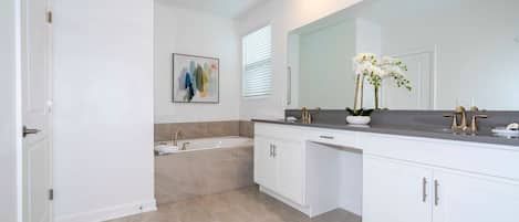 A modern bathroom with a large mirror, a bathtub, and white cabinetry.