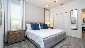 A bedroom with a large bed, a nightstand with a lamp, a dresser, a wardrobe, and a mirror on the wall.