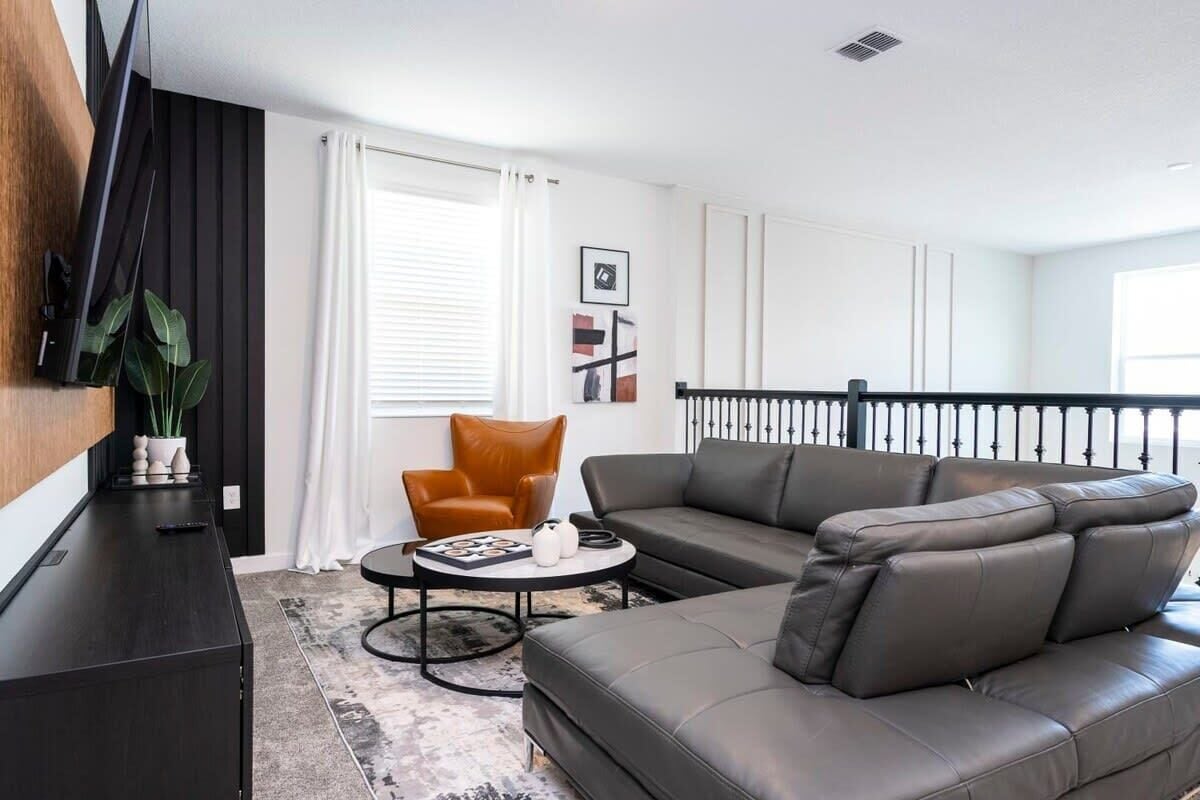 A modern living room with a dark sofa, a brown armchair, a coffee table, and a TV mounted on the wall.