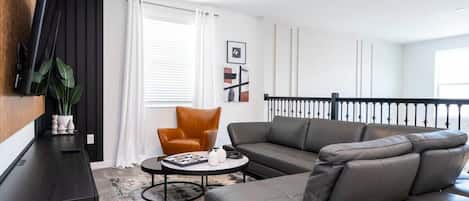 A modern living room with a dark sofa, a brown armchair, a coffee table, and a TV mounted on the wall.