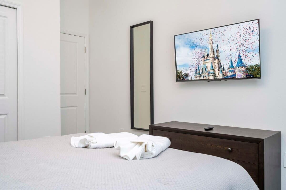 Habitación de hotel con cama, cómoda, televisor montado en la pared y un cuadro de un castillo.