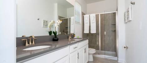 A modern bathroom with a large mirror, two sinks, a shower, and a toilet.