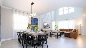 Uma sala de estar moderna com área de jantar, destacando uma mesa grande, cadeiras, um sofá e uma televisão.