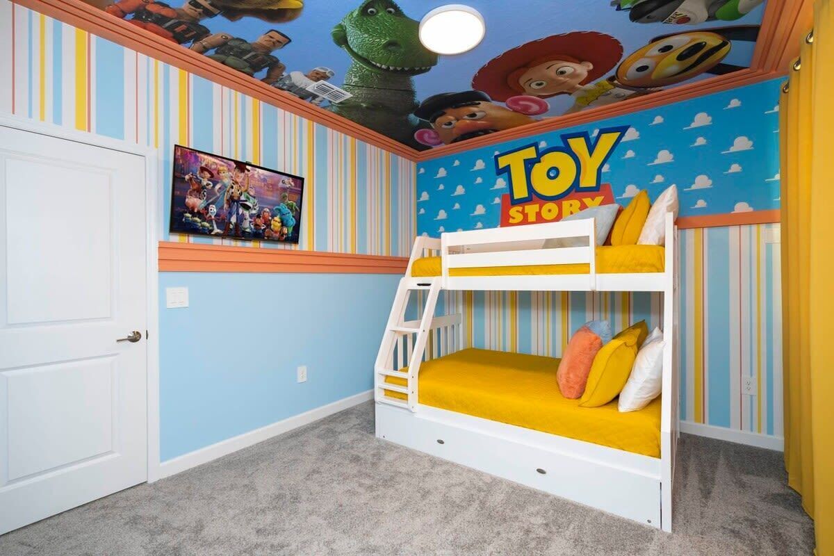 A child's bedroom with a bunk bed, a 'Toy Story' themed wall, and a TV on the wall.