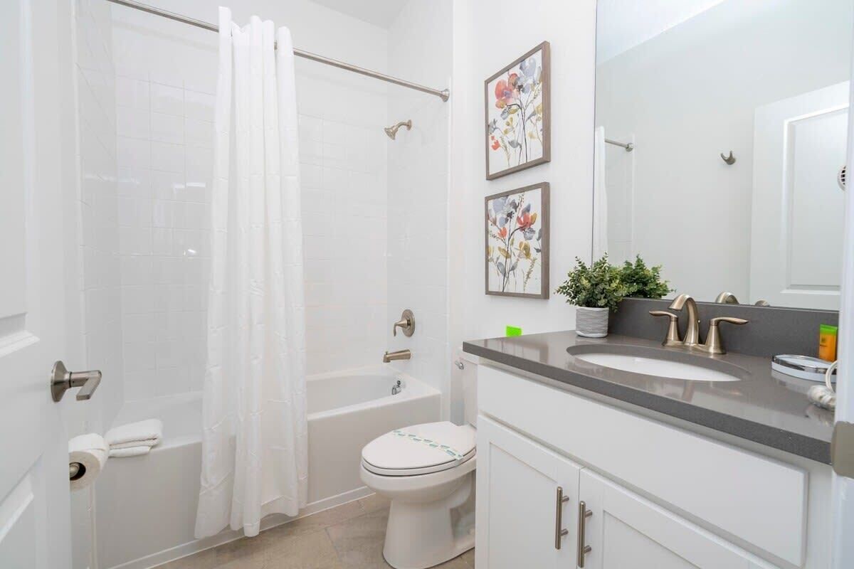 A modern bathroom with a bathtub, toilet, and sink. There are two framed floral paintings on the wall.