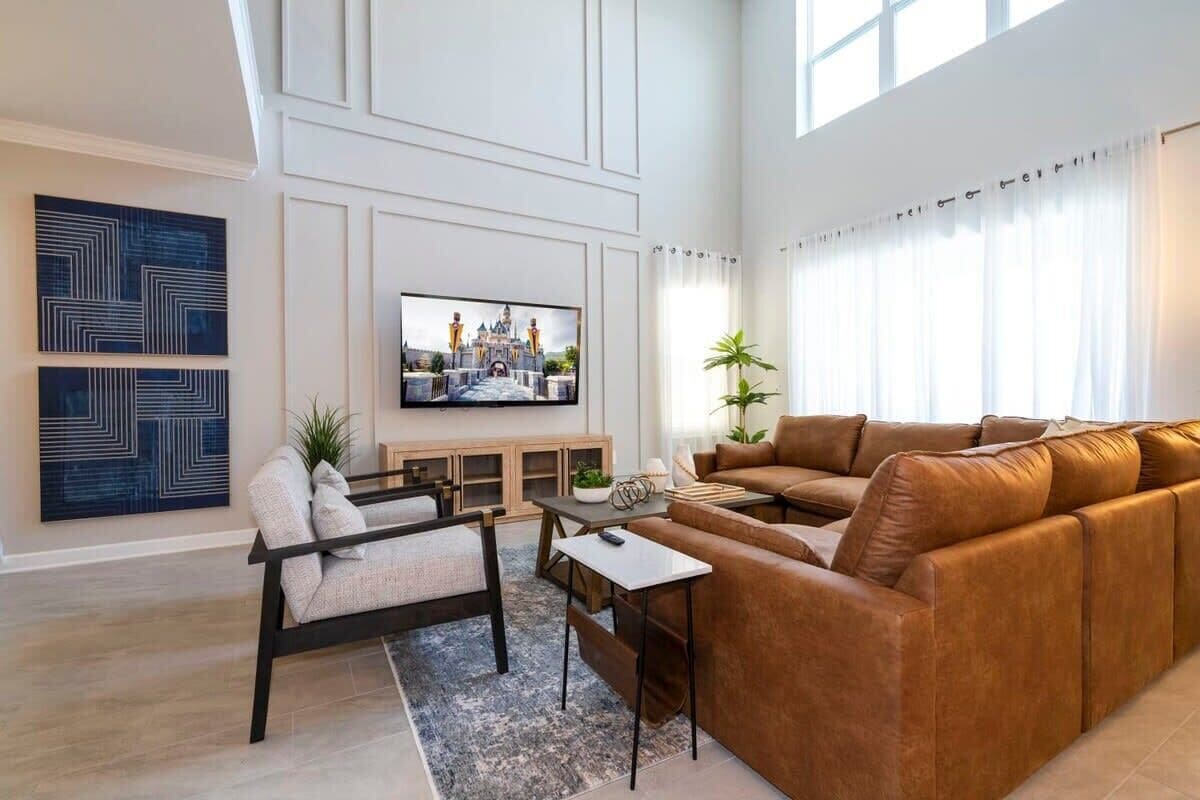 Ein modernes Wohnzimmer mit einem großen Flachbildfernseher, einem braunen Ledersofa, einem weißen Sessel und einem Couchtisch.
