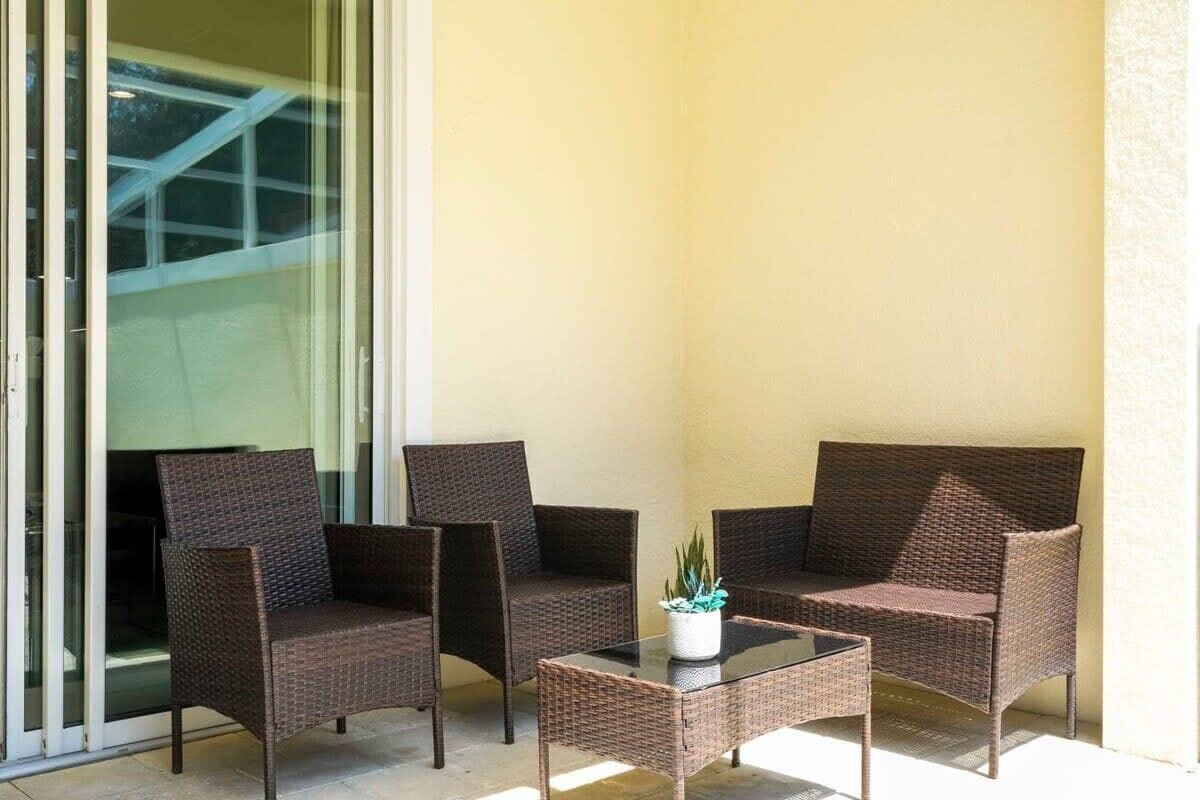 A balcony with wicker furniture, a glass table, and a potted plant.