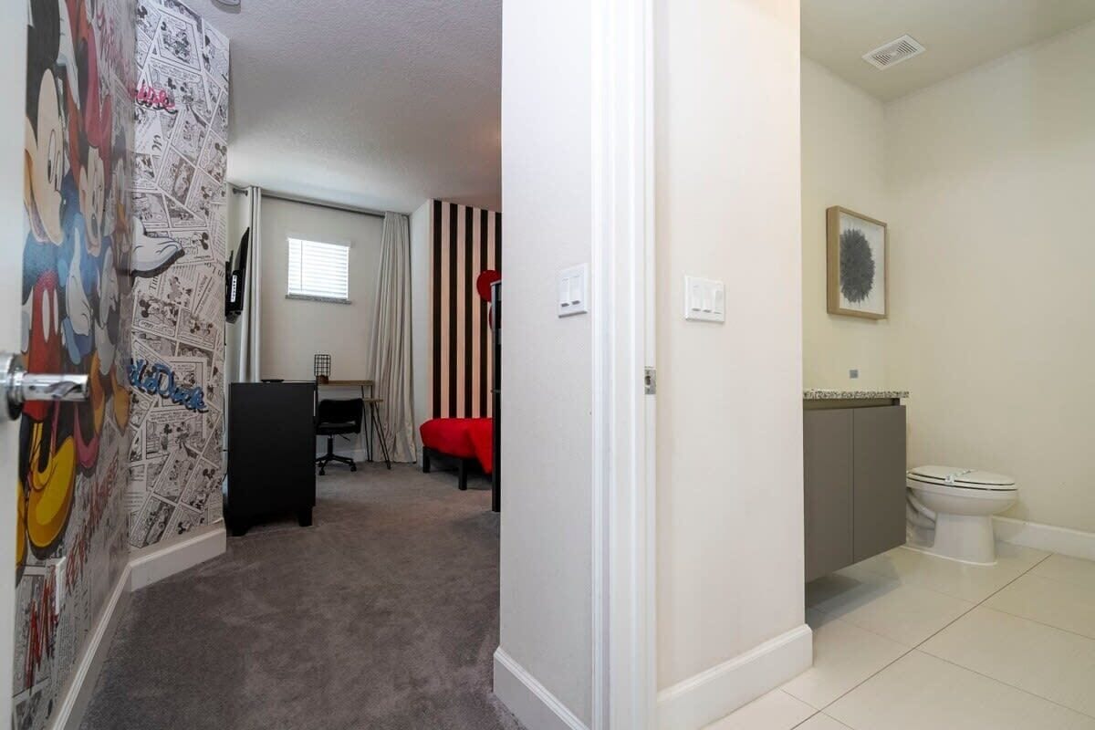 A room with a cartoon-themed wall, a desk, a chair, a striped curtain, and a toilet.