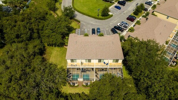An aerial view of a two-story building with a swimming pool, surrounded by trees and a parking lot.