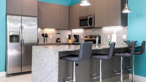 A modern kitchen with a granite countertop, stainless steel appliances, and bar stools. - Marvelous 3Bd w/ Pool Near Disney at Serenity 1536 (Clermont)