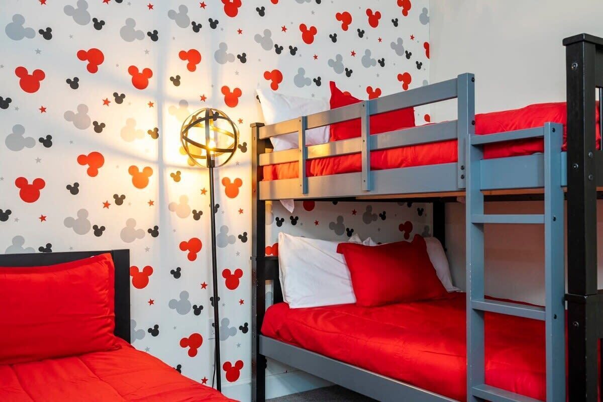 A bunk bed room with red bedding and Mickey Mouse themed wallpaper.