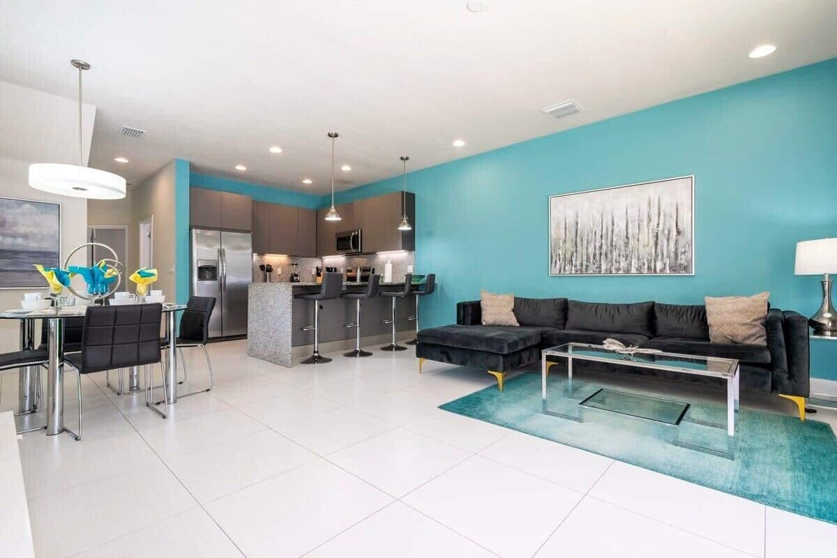 A modern living room with a black sofa, a glass coffee table, and a kitchen in the background.