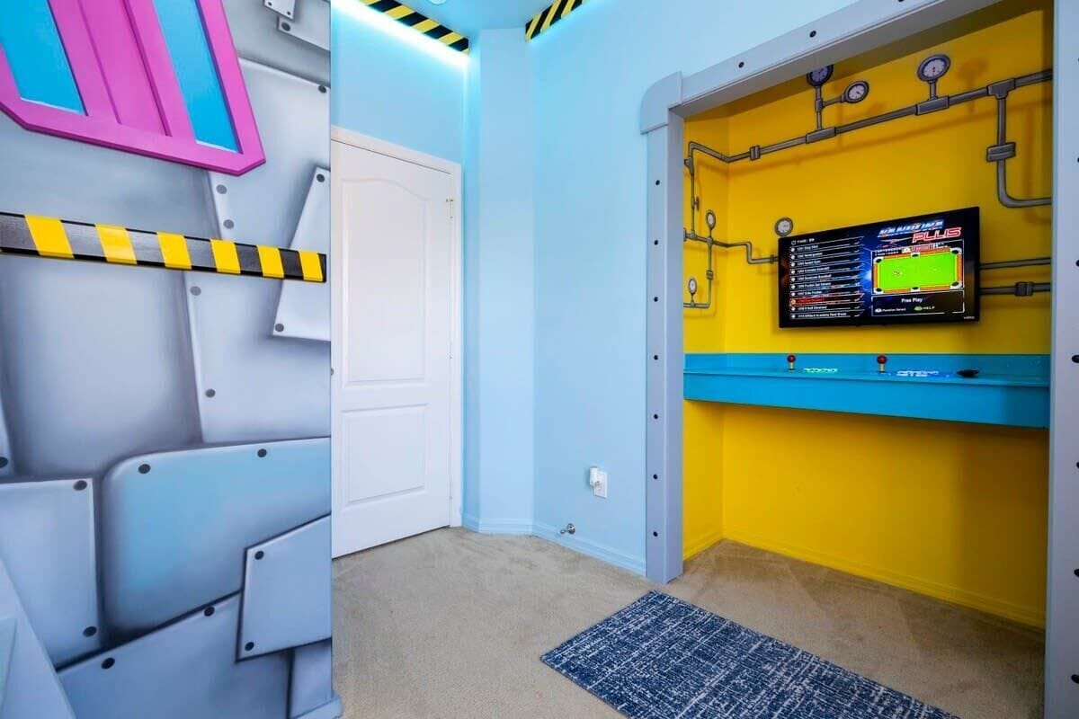 Ein Zimmer mit weißer Tür, blauer Wand, gelber Wand mit montiertem Fernseher und blauem Teppich.