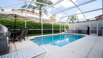 An indoor swimming pool with a covered patio area, a grill, and a table with chairs.