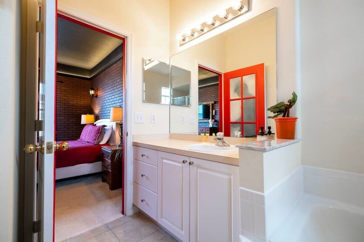 A hotel room with a bed, a bathroom with a sink and mirror, and a red-framed door.
