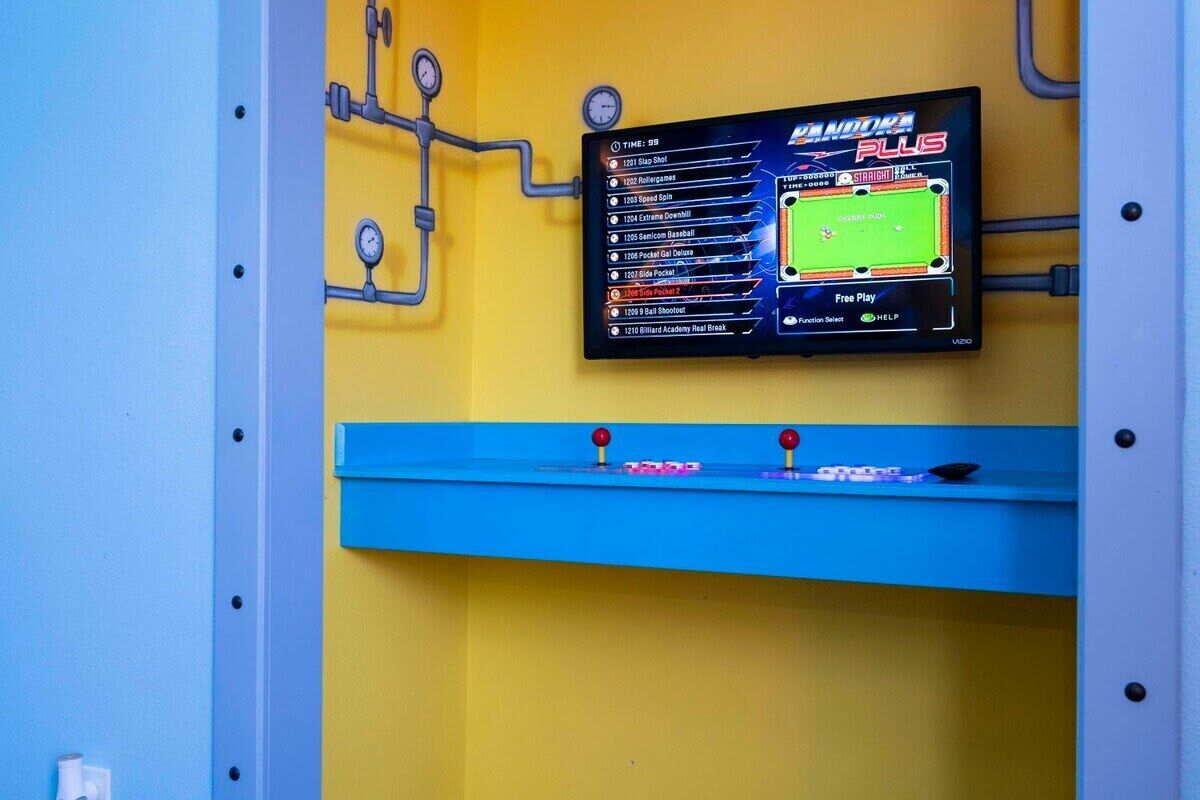 A wall-mounted digital scoreboard displaying various game scores and a "Free Play" option.