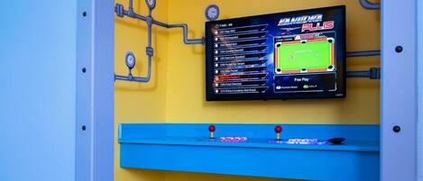 A wall-mounted digital scoreboard displaying various game scores and a "Free Play" option.
