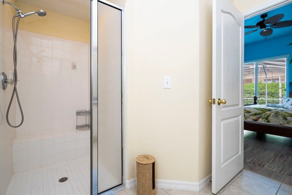 Een badkamer met een douche, een deur naar een slaapkamer en een plafondventilator.